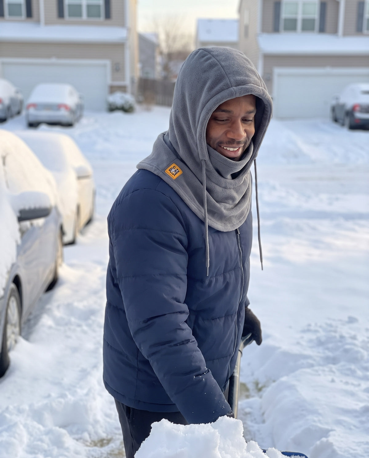 Man shoveling snow wearing the gray fleece hood as a neck warmer