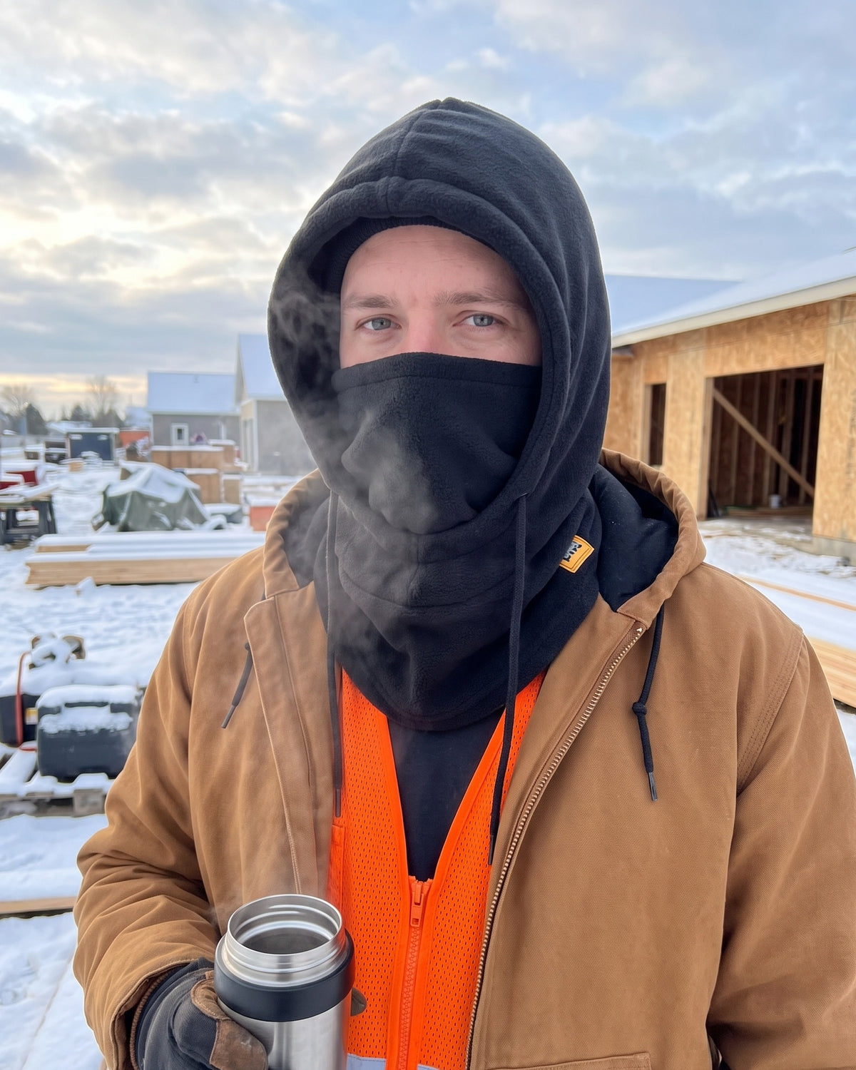Construction worker on a snowy job site wearing the black fleece hood with the mask up